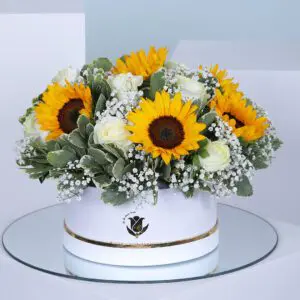 A circular box filled with a bouquet of bright yellow sunflowers and white roses.