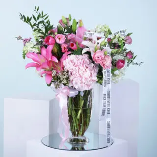 Pink flower arrangement with lilies, tulips, hydrangeas, and other blooms in a glass vase.