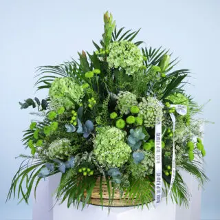 A lush arrangement of green hydrangeas, chrysanthemums, and other greenery in a woven basket.