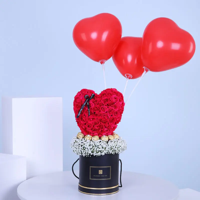 02 A black box with red roses in a heart shape, surrounded by white baby's breath, topped with three red heart-shaped balloons.