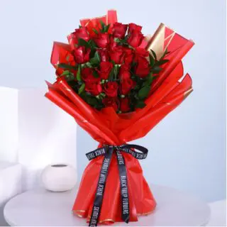 A bouquet of a dozen red roses wrapped in red tied with a black ribbon.