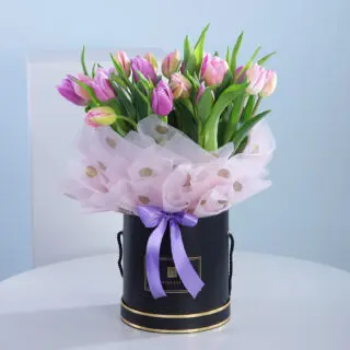 A bouquet of pink and purple tulips in a black hat box with a lilac ribbon