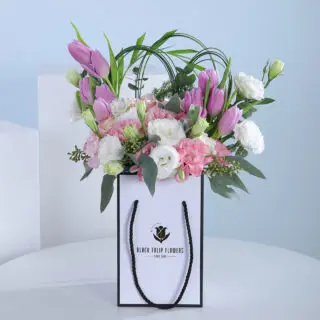 A bouquet of pink and white flowers, including tulips and eustoma, arranged in a white paper bag