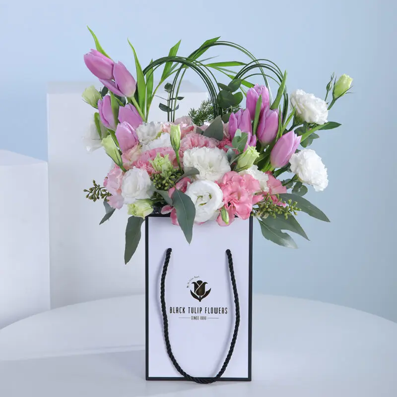 01 A bouquet of pink and white flowers, including tulips and eustoma, arranged in a white paper bag