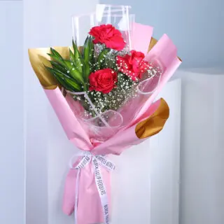 A bouquet of red roses wrapped in pink and gold paper with a white ribbon.