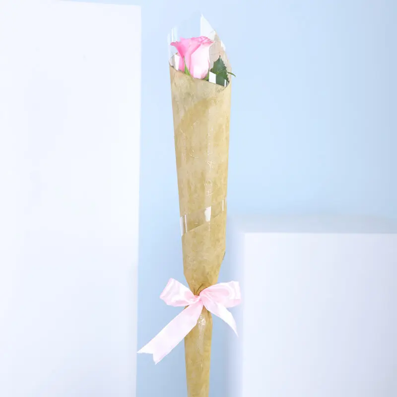 01 A single baby pink rose wrapped in paper with a pink ribbon.