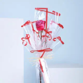 A single rose wrapped in cellophane with red ribbons.