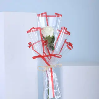 A single white rose in clear wrapping with red ribbons.