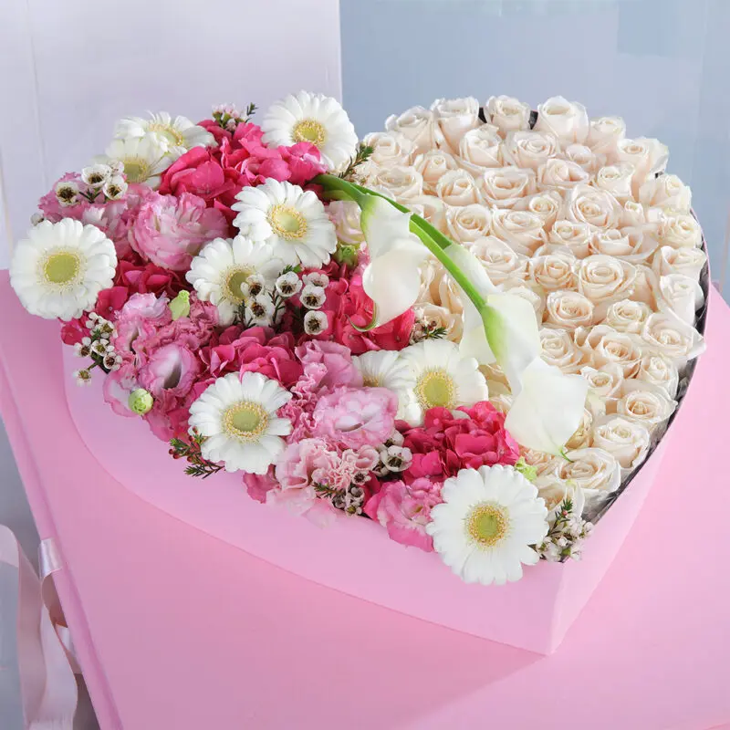 03 A heart-shaped arrangement of white roses, pink hydrangeas, white daisies, and white calla lilies in a pink box.