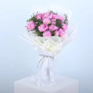 A bouquet of pink peonies wrapped in white paper, tied with a ribbon.