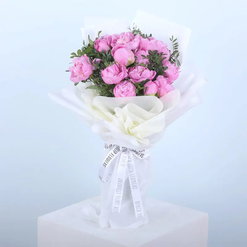 01 A bouquet of pink peonies wrapped in white paper, tied with a ribbon.