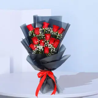 A bouquet of a dozen red roses surrounded by baby's breath, wrapped in black paper and tied with a red ribbon.