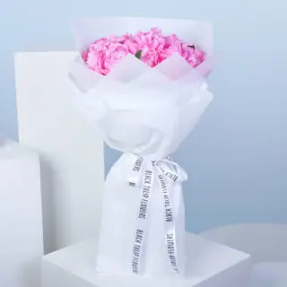 A bouquet of pink peonies wrapped in white paper, tied with a white ribbon.