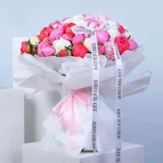 A large bouquet of pink and white peonies wrapped in white paper, tied with a pink ribbon.