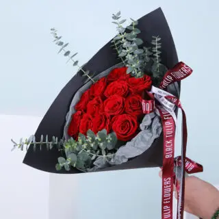 A vibrant mix of Explorer roses paired with fresh eucalyptus, elegantly wrapped in black and tied with white and maroon ribbon