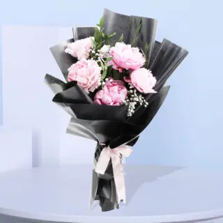 A bouquet of pink peonies and baby's breath wrapped in black paper with a pink ribbon.