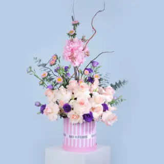 Peach rose, pink hydrangea, purple lisianthus, chrysanthemum, and eucalyptus arranged in a pink box.