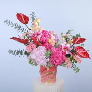 Pink hydrangeas, red anthuriums, pink roses, lilies, and eucalyptus in a marble design pink vase.