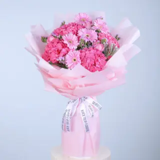 A pink bouquet of delicate gerberas, fragrant carnations, and lush hydrangeas, wrapped in pink tissue paper.