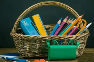 A wicker gift basket filled with school supplies, including pencils, crayons, scissors, and a ruler.