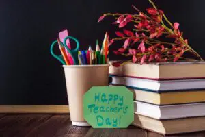 A stack of books, a cup of stationery, and a note that says Happy Teacher's Day