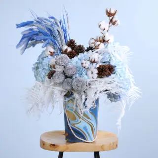 A flower centerpiece with blue hydrangeas, pine cones, cotton, ping pong balls, and dry feathers.