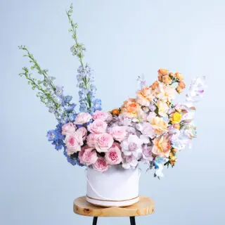 Floral arrangement with 20 Ohara roses, purple roses, peach roses, peach baby roses, and delphinium in a white flower box.