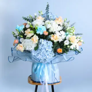  colorful bouquet of blue and white hydrangeas with peach roses, blue roses, and chrysanthemums on a wooden stool
