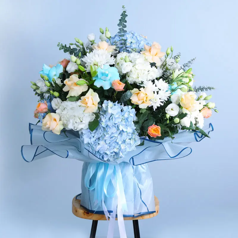 Ethereal Blue & Peach Floral Symphony colorful bouquet of blue and white hydrangeas with peach roses, blue roses, and chrysanthemums on a wooden stool