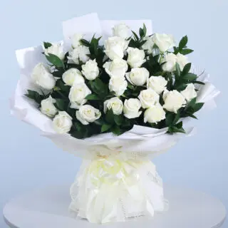 Bouquet of 30 white roses with fresh green leaves in a white wrap and tied with a white ribbon.