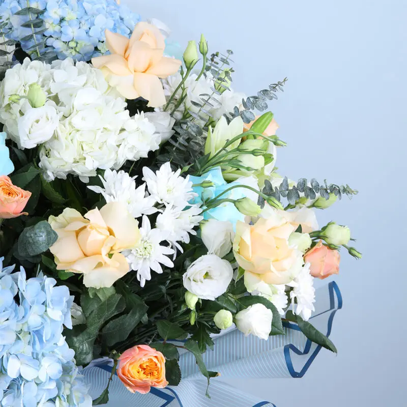 03 - Ethereal Blue & Peach Floral Symphony Blue hydrangea and peach rose bouquet with eucalyptus and lisianthus accents.