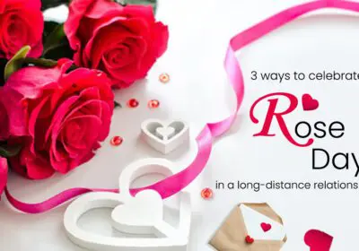 A bouquet of red roses arranged on a white surface with a pink ribbon, white hearts, and a small envelope with a red heart. The text "3 ways to celebrate a Rose Day in a long-distance relationship" is also included
