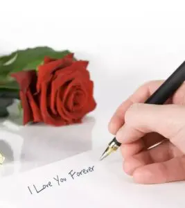 A hand writes the words "I love you forever" on a white page, framed by a beautiful red rose in the backdrop.