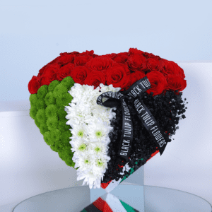 A heart-shaped arrangement of red roses, green chrysanthemums, and white flowers, designed in the colors of the UAE flag. The arrangement is tied with a black ribbon and includes the text "BLACK TULIP FLOWERS.