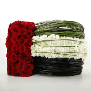 A floral arrangement designed in the colors of the UAE flag: red, green, white, and black. The arrangement features red roses, white hydrangeas, and green grass-like elements, arranged in a circular shape.