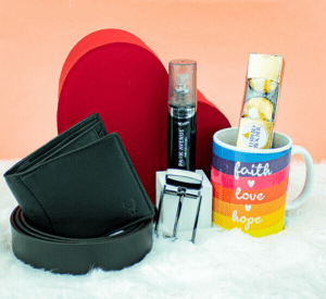 A Valentine's Day gift basket containing a leather wallet, belt, a bottle of perfume, a mug with the words "Faith, Love, Hope" printed on it, a heart-shaped box of chocolates, and a Ferrero Rocher chocolate box.