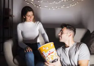 attractive smiling woman handsome positive man watching tv eating popcorn sofa scaled