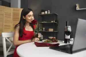 A young woman with a joyful expression is seated at a table, enjoying a virtual dinner date