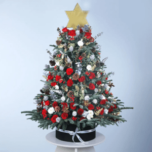 A beautiful Christmas tree made entirely of flowers. The tree is adorned with red roses, white flowers, pine cones, and gold accents. A gold star tops the tree, which is sitting in a black pot.