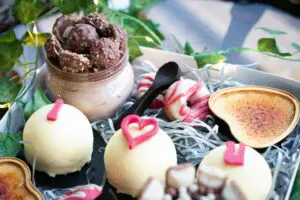 A Valentine's Day gift filled with various treats, including chocolate truffles, a donut, a crème brûlée, and a chocolate dessert in a jar