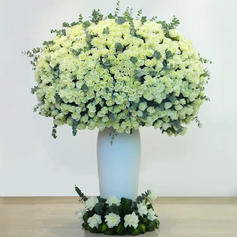 White -roses - grand-arrangement A large, round arrangement of luxurious white roses and greenery, overflowing from a tall, white vase.