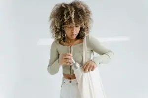 A woman with curly hair proudly displays an eco-friendly tote bag, emphasizing her commitment to sustainability.