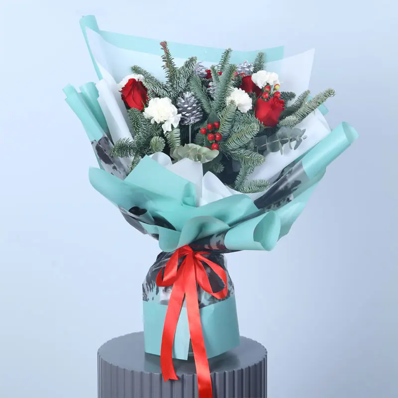 A snowy day bouquet with white carnations, pine cones, and greenery, wrapped in blue paper.