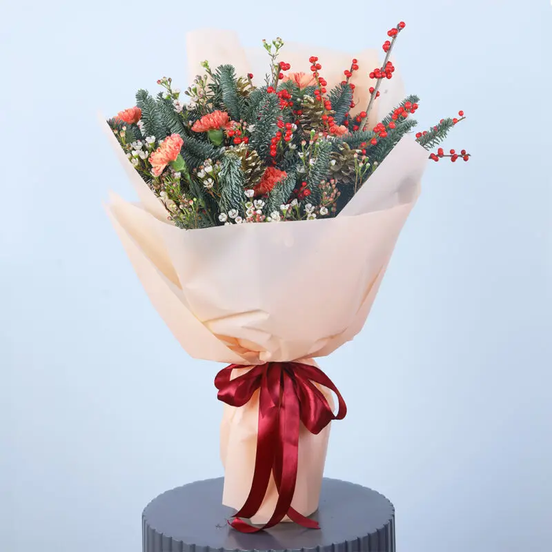 holiday-cheer-christmas-bouquet Christmas bouquet with red carnations, greenery, pinecones, and holly berries in a stylish arrangement.