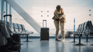 In an airport terminal, a man and woman share a warm hug, symbolizing a long-distance reunion filled with emotion.