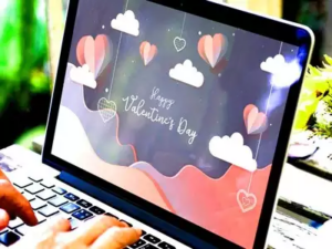 A laptop screen displaying a Valentine's Day themed wallpaper with heart-shaped balloons and the message "Happy Valentine's Day". A person is typing on the laptop keyboard.