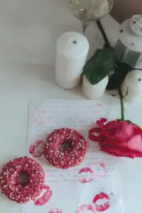 A romantic scene with pink donuts, a handwritten love letter, a red rose, and candles creating a cozy atmosphere.
