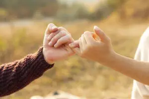 Two people linking pinky fingers outdoors in a sunlit setting promise