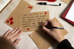 A person's hands writing a heartfelt love letter on a brown envelope. The letter expresses feelings of love and gratitude. Red hearts are drawn around the words
