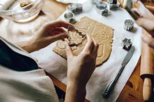 10 Last Minute Christmas Gift Ideas 4 A person uses a cookie cutter to shape dough into a cookie on a wooden surface, showcasing the baking process.